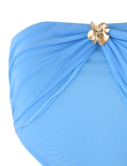 Close-up of the TIGERMIST KYNLEE DRESS in sky blue, featuring sheer mesh fabric, a strapless neckline, and a gold flower-shaped embellishment at the waist.